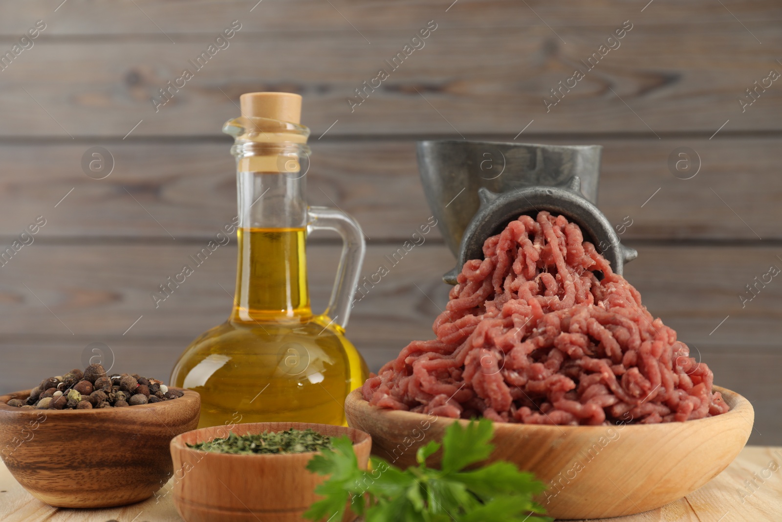 Photo of Mincing beef with manual meat grinder. Parsley, oil and spices on wooden table