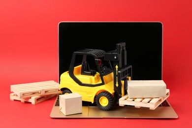 Photo of Laptop, toy forklift with wooden pallets and boxes on red background