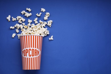 Photo of Bucket of tasty popcorn on blue background, flat lay. Space for text