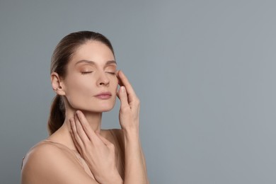 Photo of Woman massaging her face on grey background. Space for text
