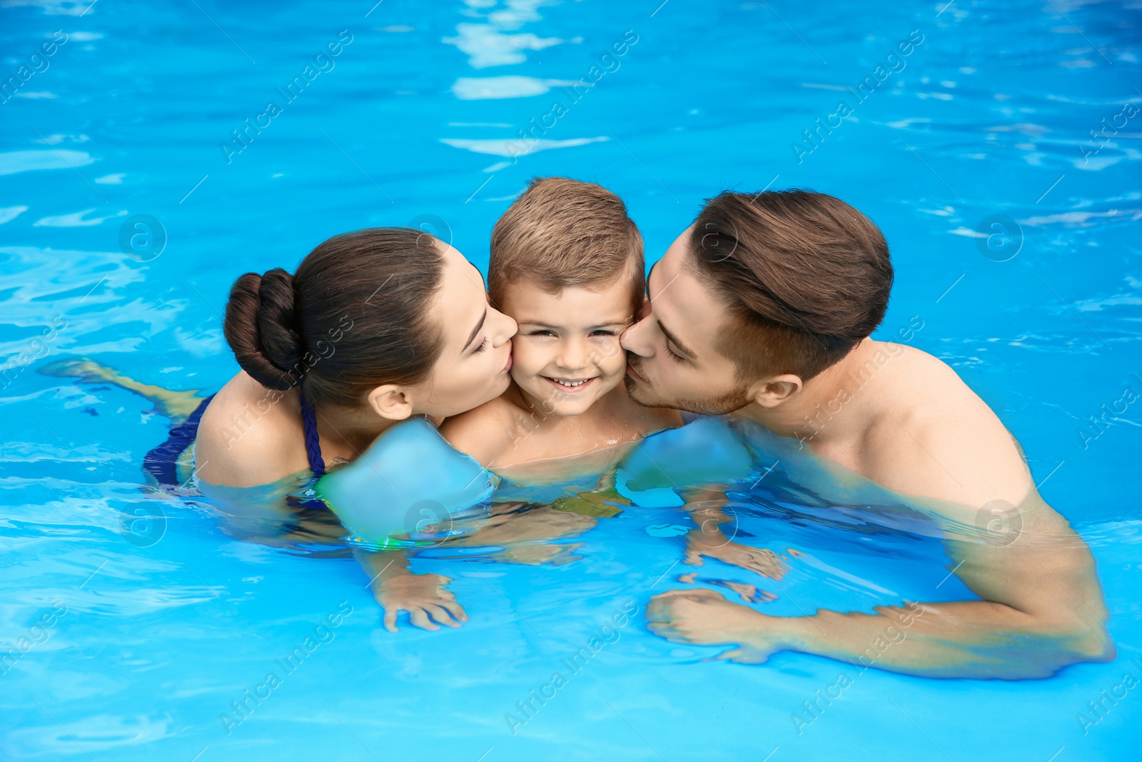 Photo of Young family with little son in swimming pool on sunny day