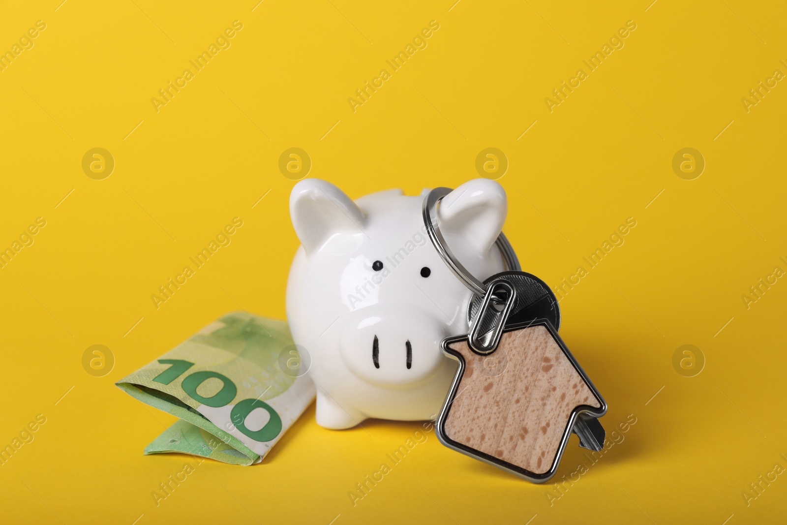 Photo of Ceramic piggy bank, euro banknote and key with trinket on yellow background. Financial savings