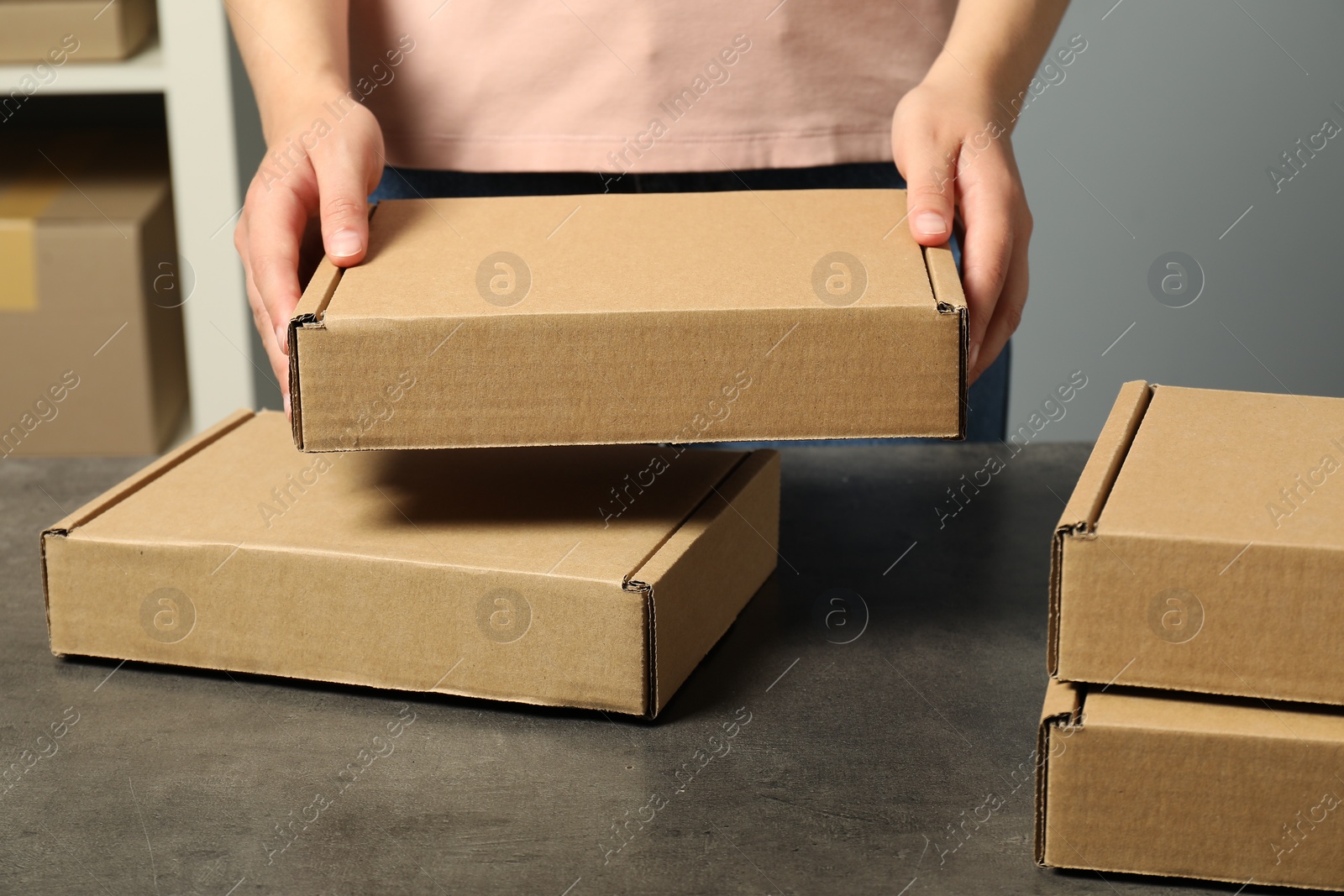 Photo of Packaging goods. Woman with cardboard boxes at grey table indoors, closeup