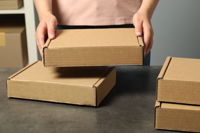 Packaging goods. Woman with cardboard boxes at grey table indoors, closeup