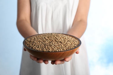 Photo of Woman holding bowl with hemp seeds on color background, closeup