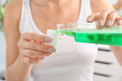 Photo of Woman pouring mouthwash from bottle into cap, closeup. Teeth care