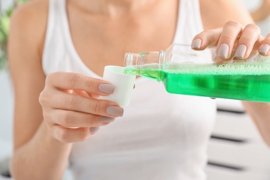 Woman pouring mouthwash from bottle into cap, closeup. Teeth care