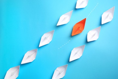 Photo of Orange paper boat floating between others on light blue background, flat lay. Uniqueness concept