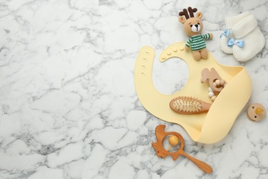 Photo of Flat lay composition with silicone baby bib, toys and accessories on white marble background. Space for text