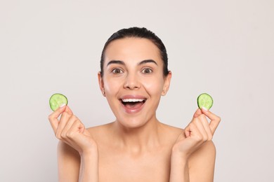 Photo of Beautiful young woman with slices of cucumber on light grey background