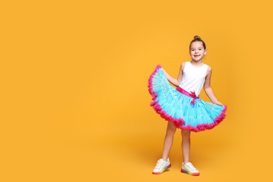 Cute little girl in tutu skirt dancing on yellow background. Space for text