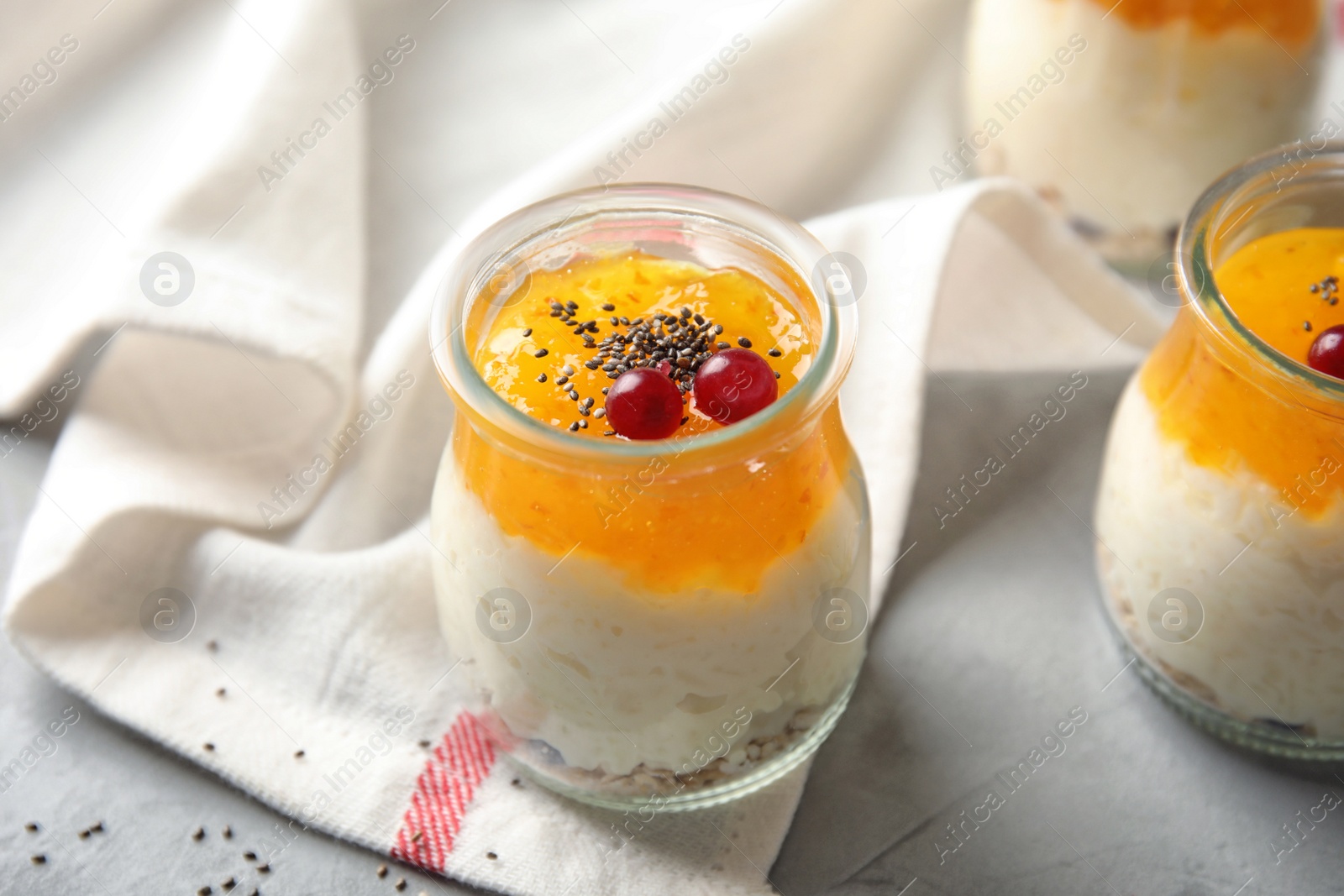 Photo of Creamy rice pudding with red currant, jam and oatmeal in jars on table