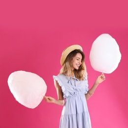 Happy young woman with cotton candies on pink background