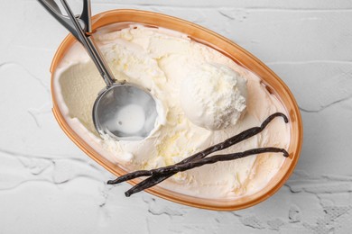 Photo of Delicious ice cream, scoop and vanilla pods in container on white textured table, top view