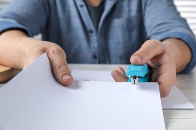 Photo of Man with papers using stapler at white table, closeup