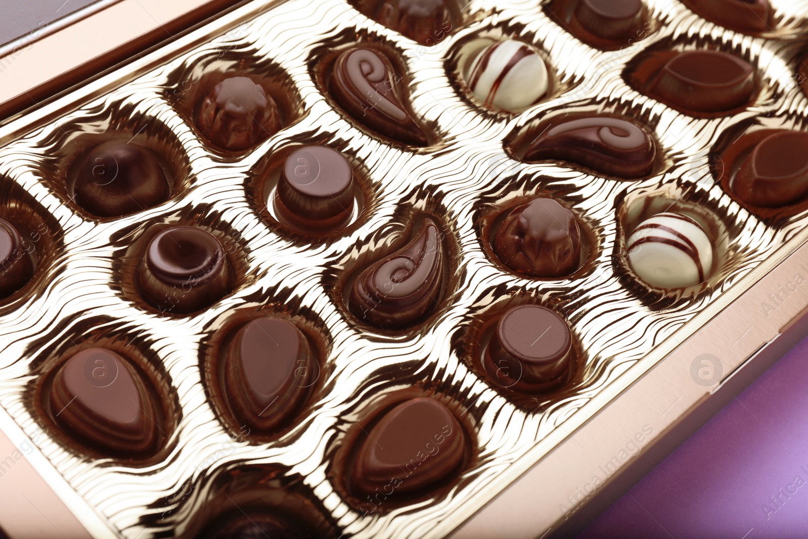 Photo of Box of delicious chocolate candies on violet background, closeup