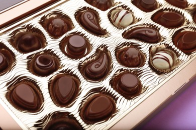 Box of delicious chocolate candies on violet background, closeup