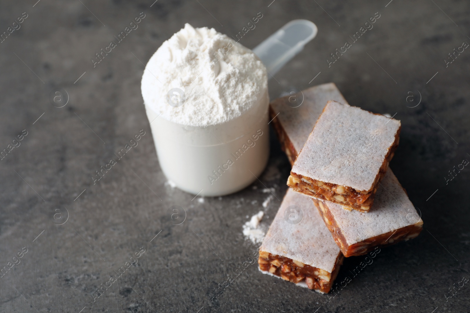 Photo of Tasty protein bars and scoop of powder on grey table. Space for text