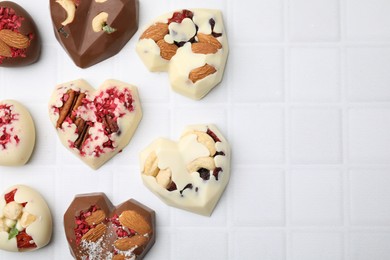 Tasty chocolate heart shaped candies with nuts on white tiled table, flat lay. Space for text