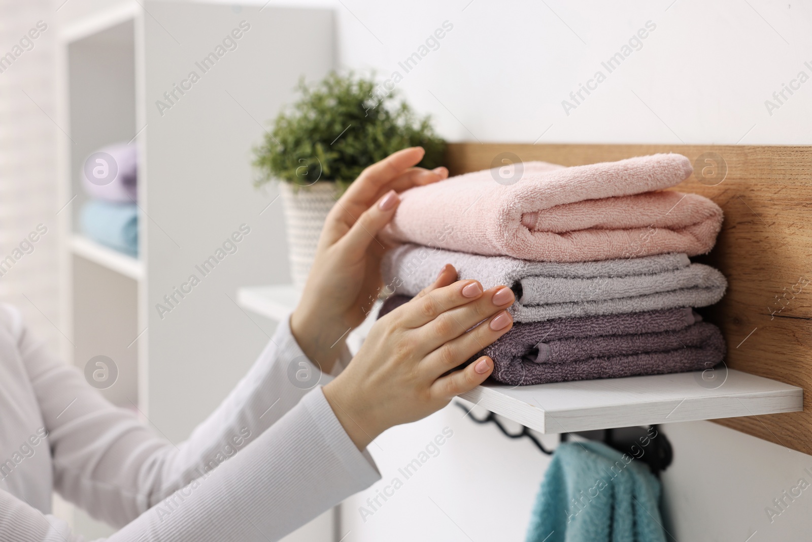 Photo of Woman stacking clean towels on shelf indoors, closeup