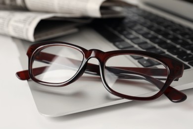 Photo of Modern laptop and glasses on white table, closeup
