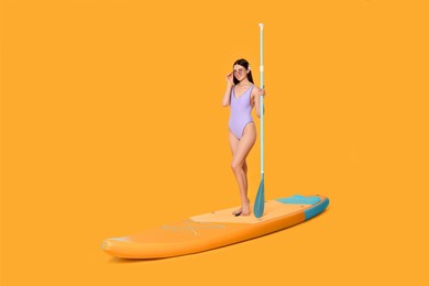 Happy woman with paddle on SUP board against orange background