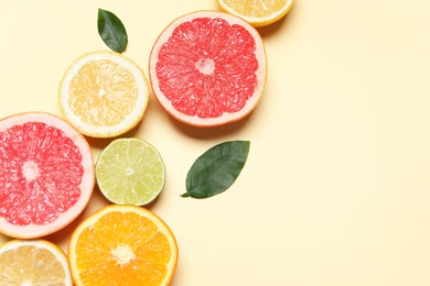 Photo of Different cut citrus fruits and leaves on beige table, flat lay. Space for text