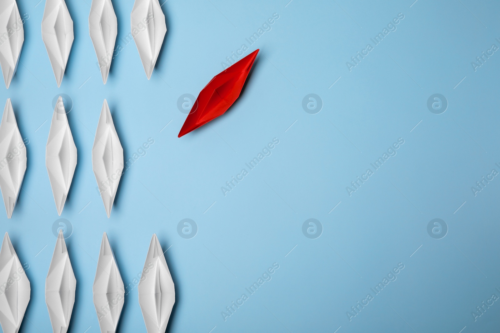 Photo of Red paper boat floating away from others on light blue background, flat lay with space for text. Uniqueness concept