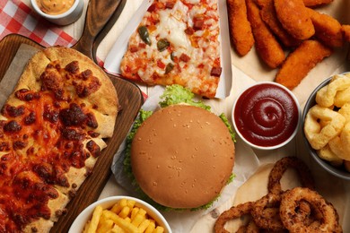 Pizza, chicken nuggets and other fast food on wooden table, flat lay
