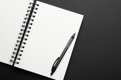 Photo of Notebook and pen on black background, top view. Space for text
