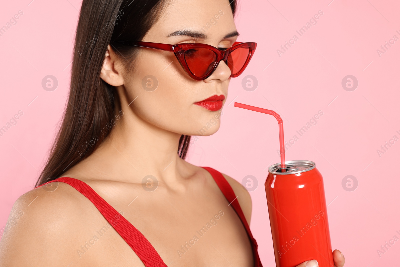 Photo of Beautiful young woman with stylish sunglasses drinking from tin can on pink background