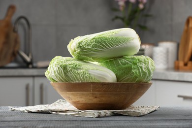 Photo of Fresh Chinese cabbages in bowl on grey wooden table indoors