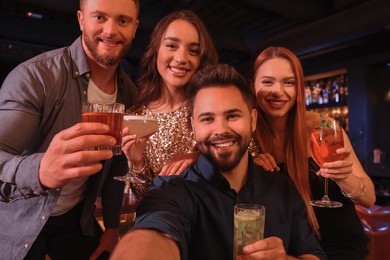 Happy friends with cocktails taking selfie together in bar