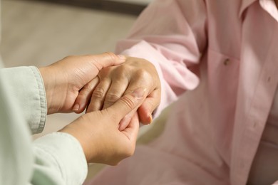 Photo of Young and elderly women holding hands indoors, closeup