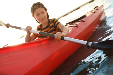 Photo of Happy little boy kayaking along river, focus on paddle. Summer camp activity