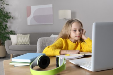 Photo of Cute little girl with modern laptop studying online at home, space for text. E-learning