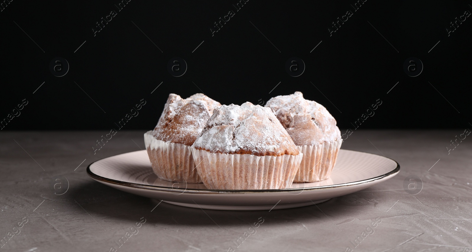 Photo of Tasty muffins with sugar powder on grey textured table, closeup