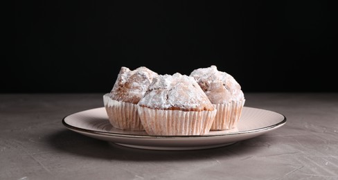 Tasty muffins with sugar powder on grey textured table, closeup