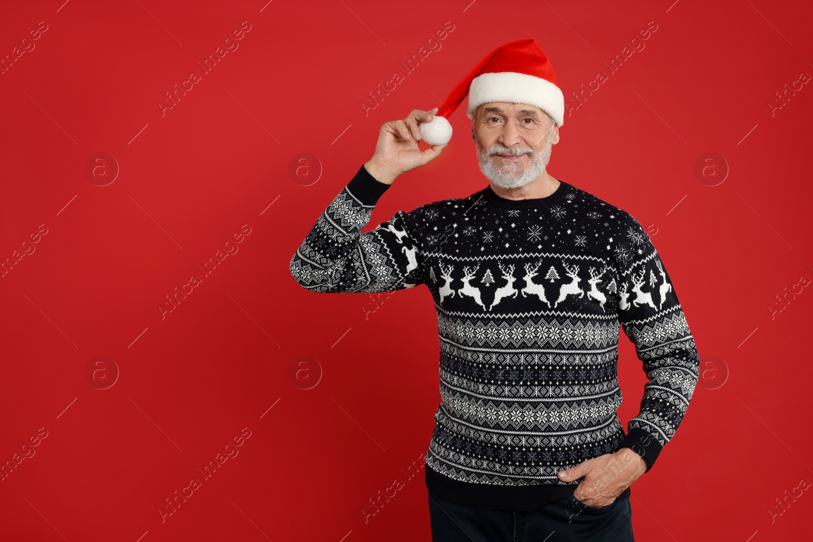 Photo of Senior man in Christmas sweater and Santa hat on red background. Space for text