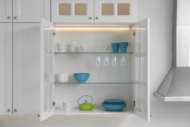 Photo of Open cabinet with different clean dishware in kitchen