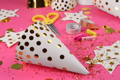 Photo of Party hat with confetti, paper stars and different materials on pink background. Handmade decorations