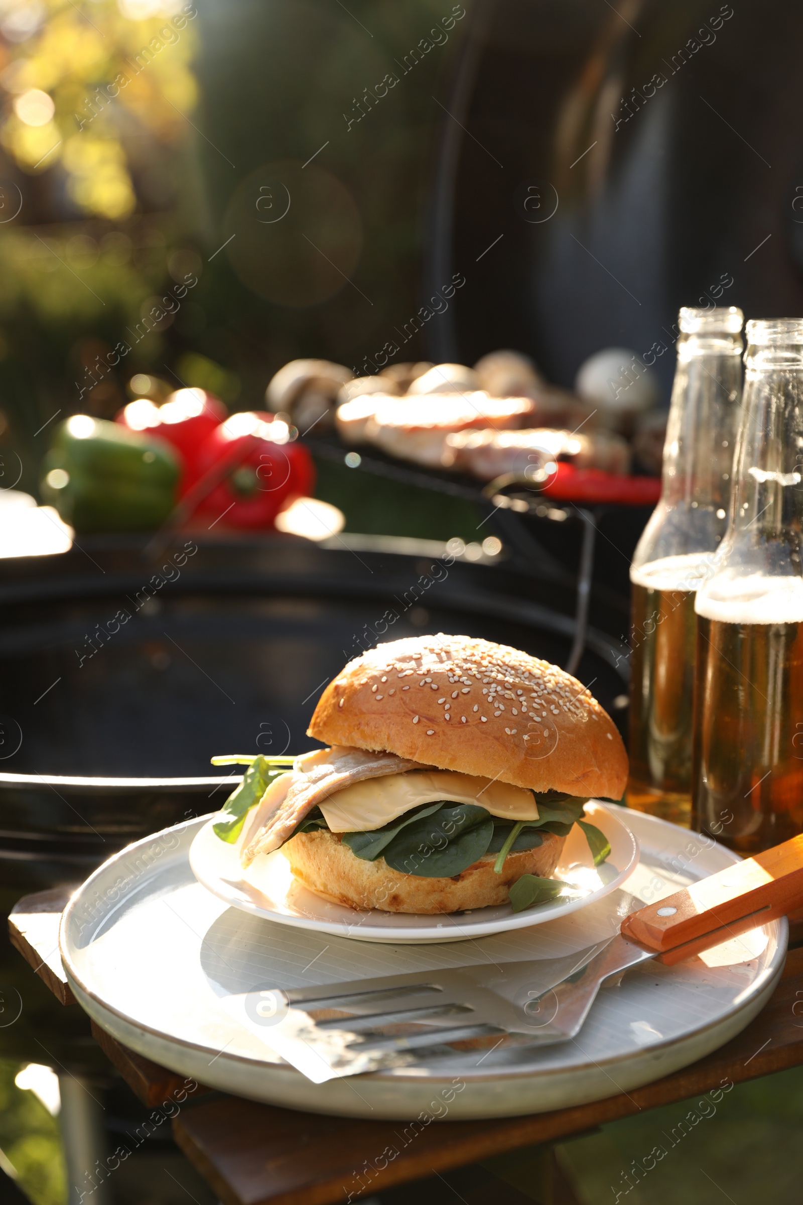 Photo of Tasty burger on table near barbecue grill outdoors. Space for text