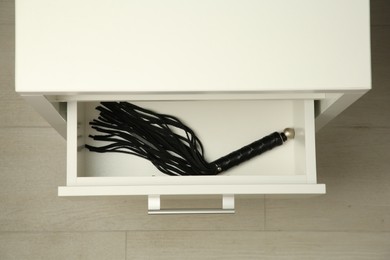 Photo of Black whip in drawer indoors, top view. Sex toy