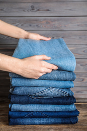Photo of Woman folding stylish jeans on wooden table, closeup