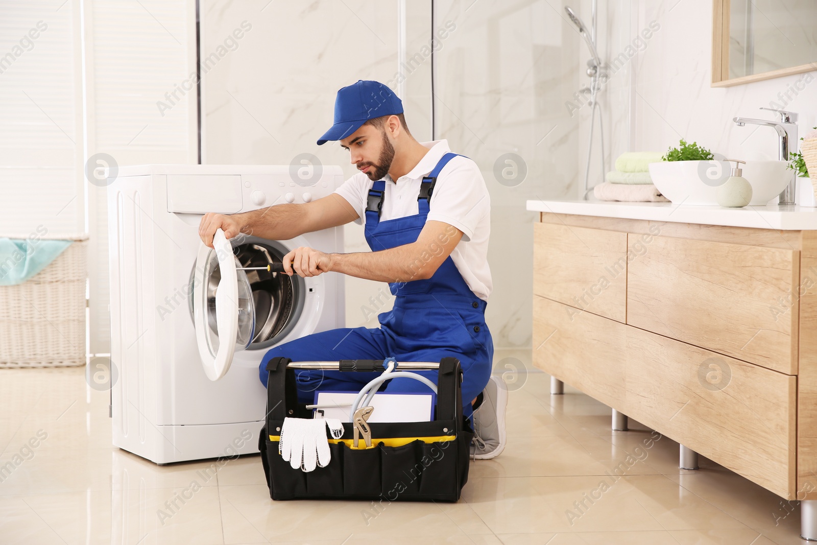 Photo of Professional plumber repairing washing machine in bathroom