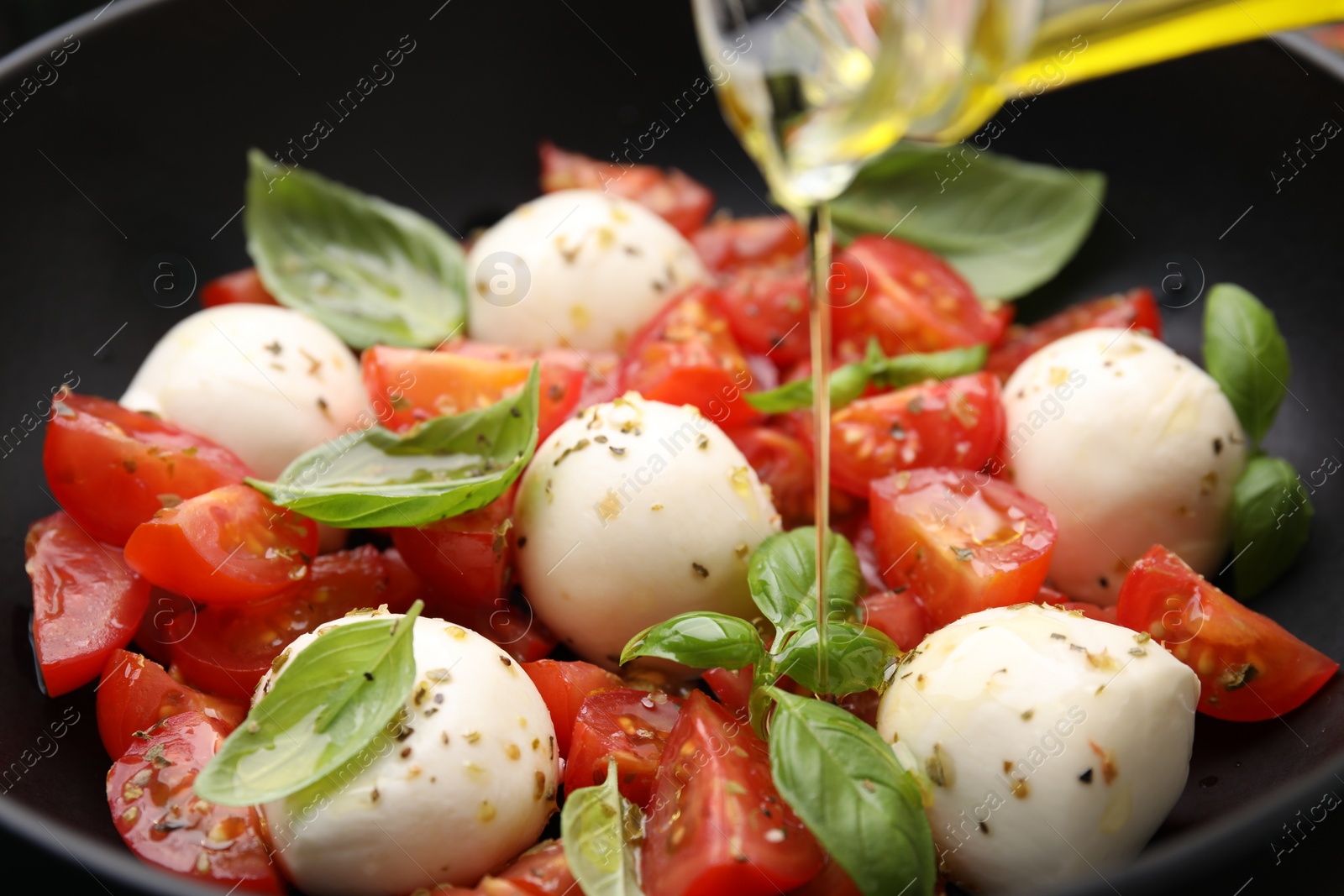 Photo of Pouring oil onto tasty salad Caprese with tomatoes, mozzarella balls and basil, closeup