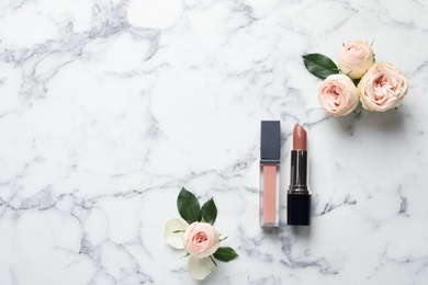 Lipstick and lip gloss with flowers on marble background, flat lay. Space for text