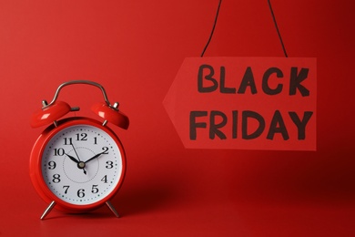 Photo of Tag with phrase Black Friday and alarm clock on red background
