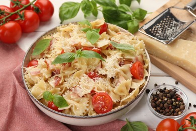 Plate of delicious pasta with tomatoes, basil and parmesan cheese near ingredients on white table