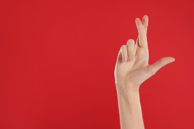 Photo of Woman with crossed fingers and space for text on red background, closeup. Superstition concept